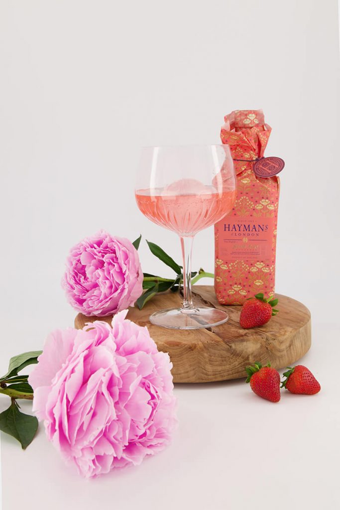 Gin bottle and glass styled with flowers and strawberries to create creative photography